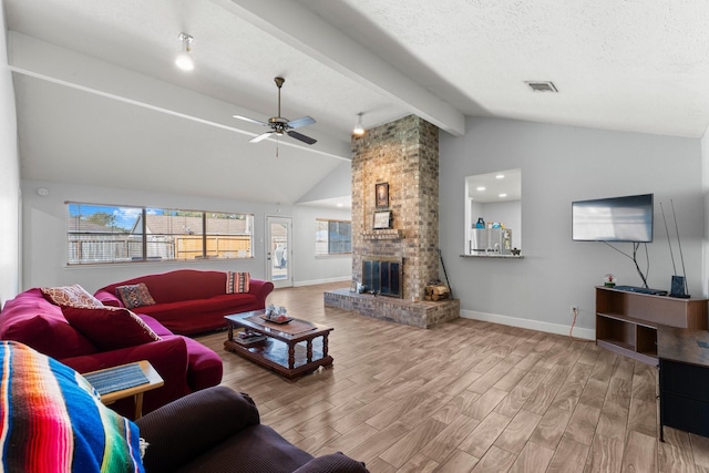 living room featuring ceiling fan, vaulted ceiling with beams, a fireplace, and a textured ceiling