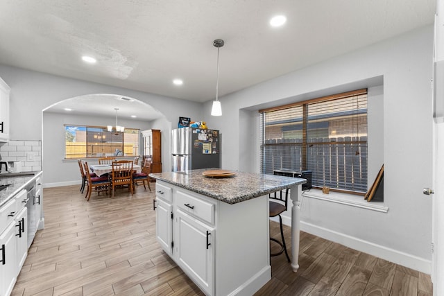 kitchen featuring stainless steel fridge, a kitchen island, pendant lighting, white cabinets, and light stone counters