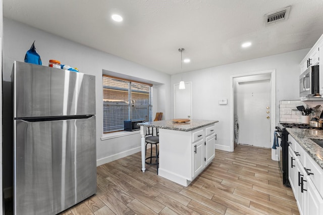 kitchen with appliances with stainless steel finishes, white cabinets, hanging light fixtures, a kitchen island, and light stone counters