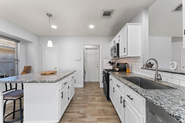 kitchen featuring appliances with stainless steel finishes, tasteful backsplash, light stone countertops, white cabinets, and sink