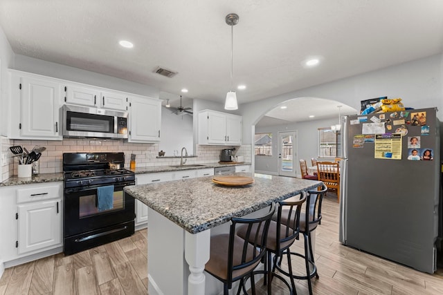 kitchen featuring appliances with stainless steel finishes, a center island, decorative light fixtures, white cabinetry, and light stone counters