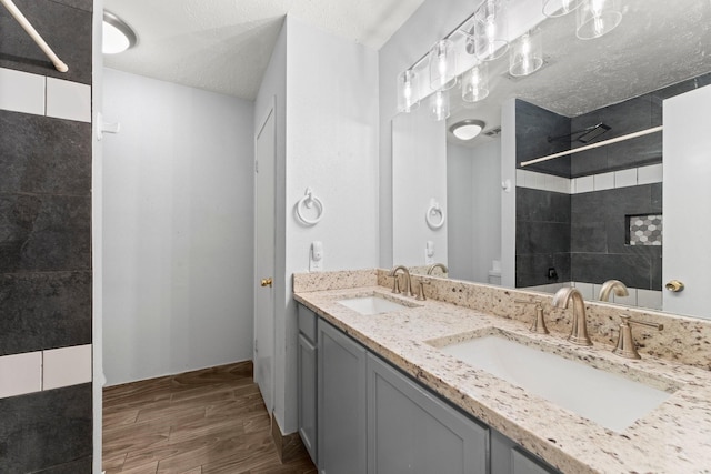 bathroom featuring a textured ceiling, tiled shower, and vanity