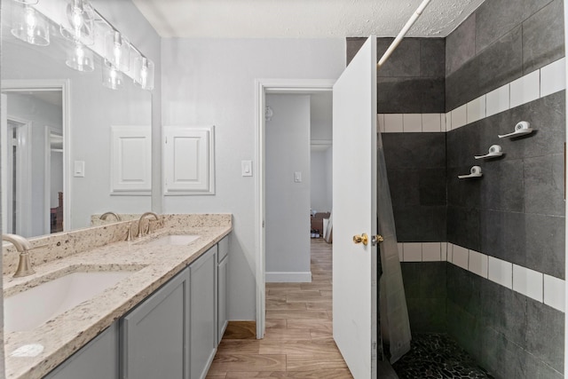 bathroom featuring vanity, wood-type flooring, tiled shower, and a textured ceiling