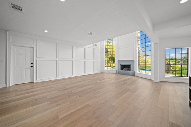 unfurnished living room featuring a healthy amount of sunlight, a textured ceiling, and light wood-type flooring