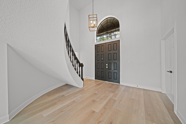 entryway featuring a chandelier, high vaulted ceiling, light hardwood / wood-style floors, and a textured ceiling