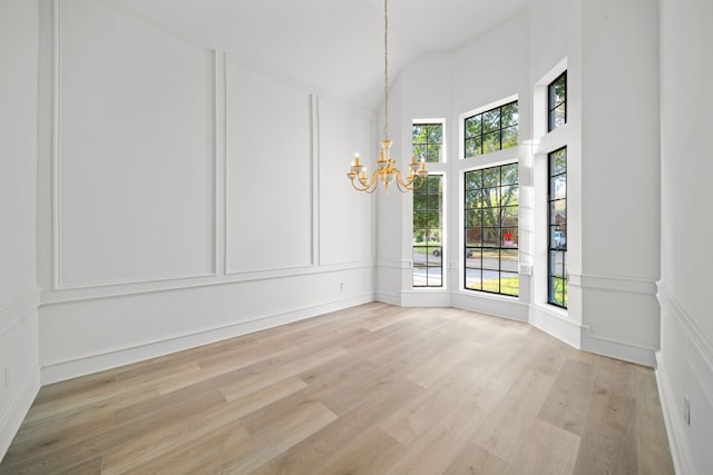 empty room with an inviting chandelier, a healthy amount of sunlight, and light wood-type flooring