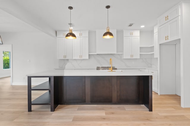 kitchen with light wood-type flooring, tasteful backsplash, premium range hood, decorative light fixtures, and white cabinets