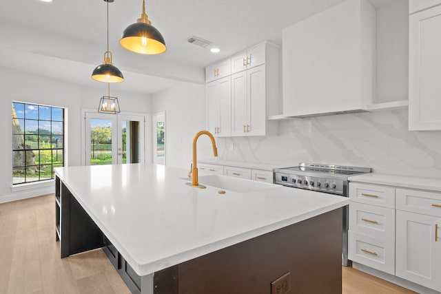 kitchen featuring pendant lighting, white cabinetry, sink, and an island with sink