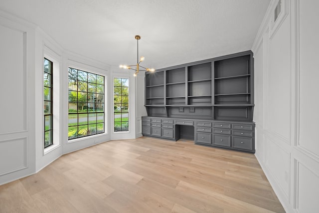 unfurnished office with crown molding, a chandelier, a textured ceiling, built in desk, and light wood-type flooring