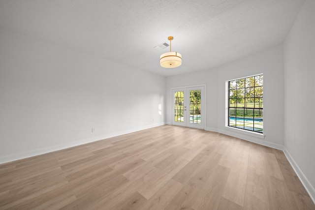 empty room featuring french doors, a textured ceiling, and light hardwood / wood-style floors