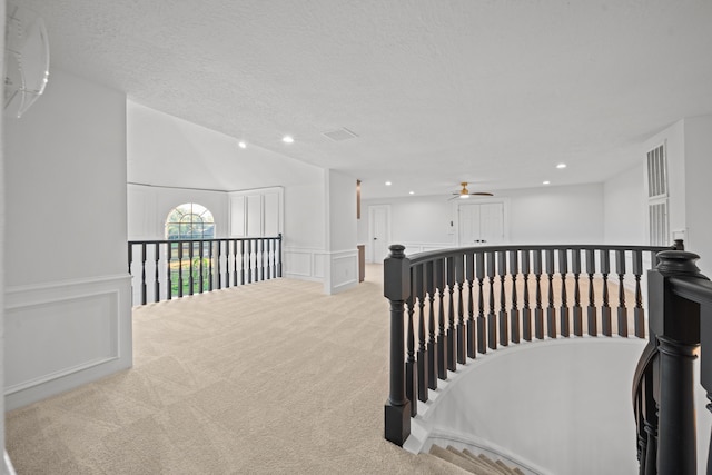 hallway featuring lofted ceiling, light colored carpet, and a textured ceiling