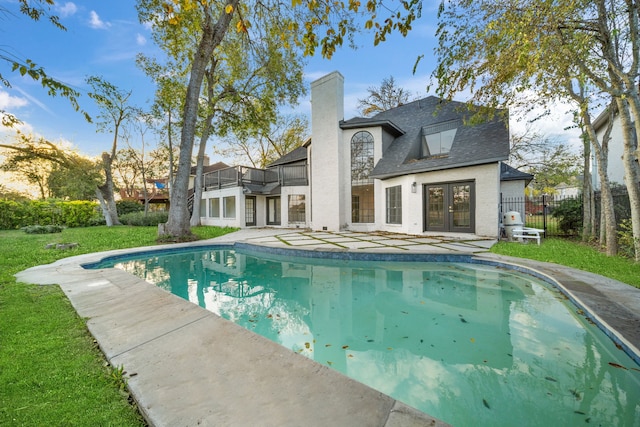 back of property with french doors, a balcony, and a lawn