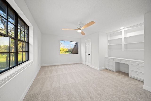 unfurnished bedroom featuring light carpet, a textured ceiling, built in desk, and ceiling fan