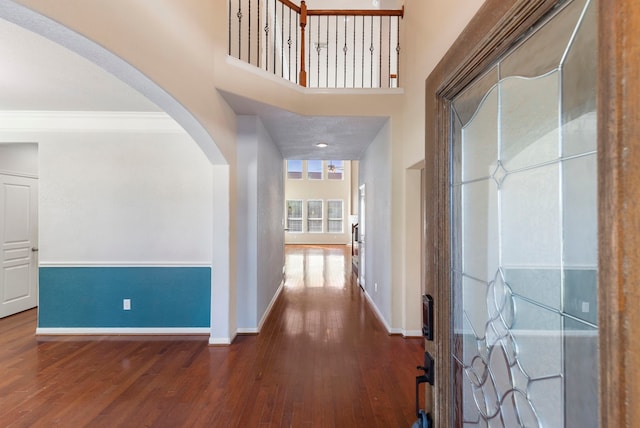 corridor with dark wood-type flooring, ornamental molding, and a towering ceiling