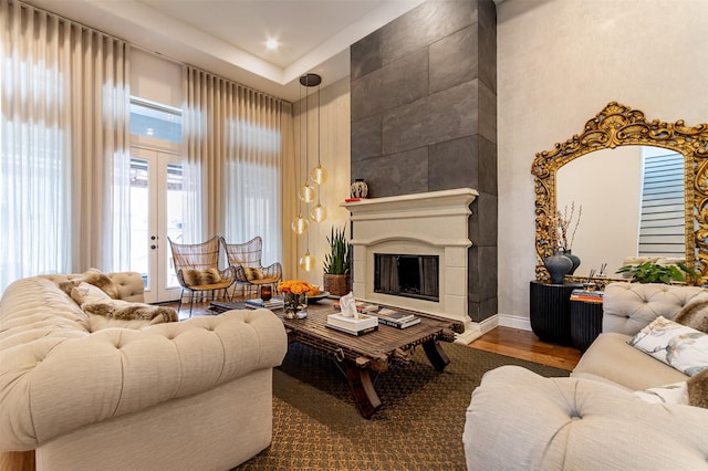 living room featuring hardwood / wood-style floors, a towering ceiling, a tile fireplace, and french doors