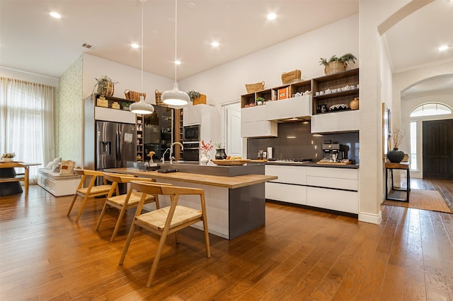 kitchen with a kitchen island with sink, hardwood / wood-style flooring, decorative light fixtures, white cabinetry, and stainless steel appliances