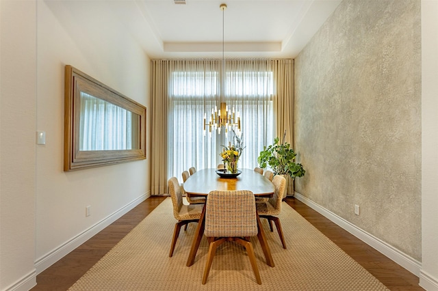 dining area featuring a raised ceiling, dark wood-type flooring, and a notable chandelier