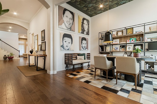 sitting room with crown molding, a high ceiling, arched walkways, and wood finished floors