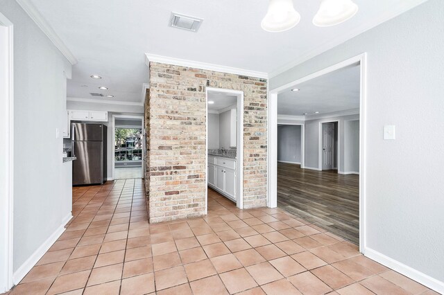 unfurnished room with light tile patterned flooring, brick wall, and ornamental molding