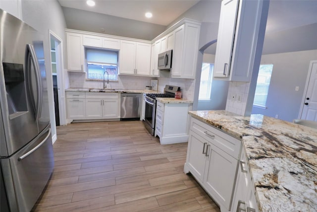 kitchen featuring tasteful backsplash, stainless steel appliances, sink, white cabinets, and light hardwood / wood-style floors