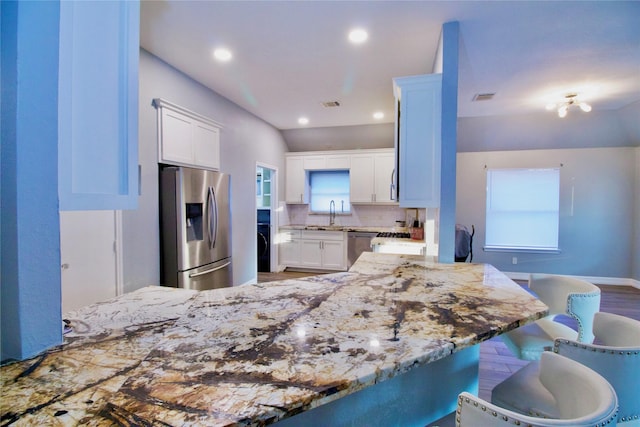 kitchen featuring decorative backsplash, kitchen peninsula, a kitchen bar, stainless steel appliances, and white cabinetry