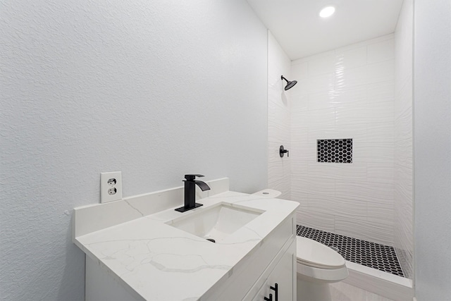 bathroom with tiled shower, vanity, and toilet