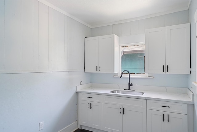 kitchen with white cabinets, light stone countertops, ornamental molding, and sink