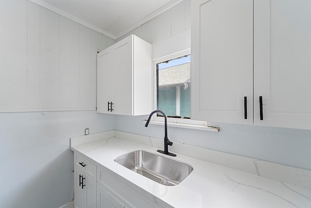 kitchen with light stone counters, crown molding, white cabinetry, and sink