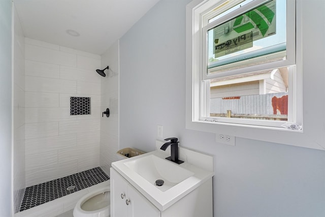 bathroom with toilet, a tile shower, and vanity