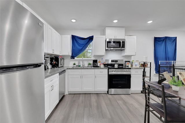 kitchen featuring stainless steel appliances, white cabinetry, light stone countertops, and sink