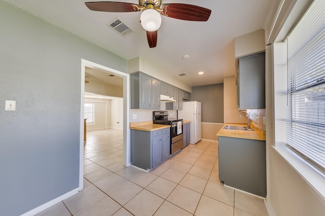 kitchen with light tile patterned flooring, gray cabinets, white fridge, and electric stove