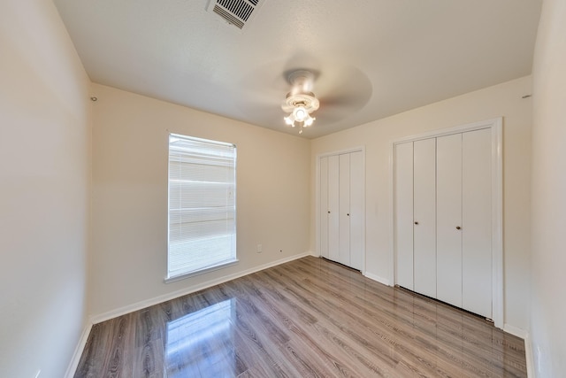 unfurnished bedroom with light hardwood / wood-style flooring, ceiling fan, and multiple closets