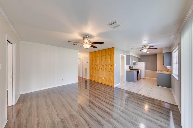 unfurnished living room with ceiling fan, sink, ornamental molding, and light wood-type flooring