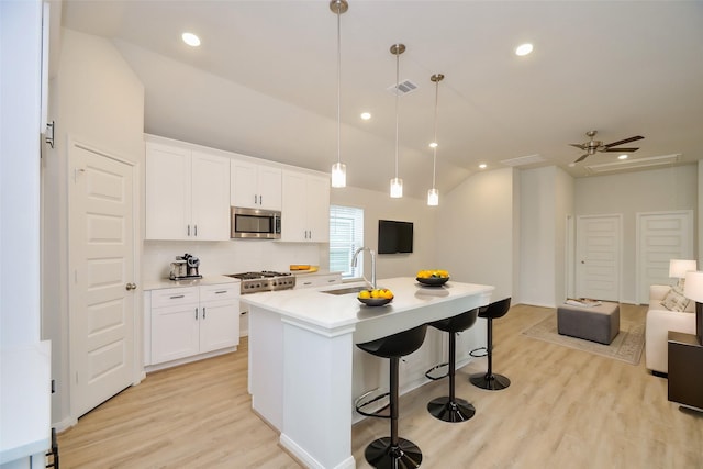 kitchen featuring a breakfast bar, sink, white cabinetry, a center island with sink, and pendant lighting