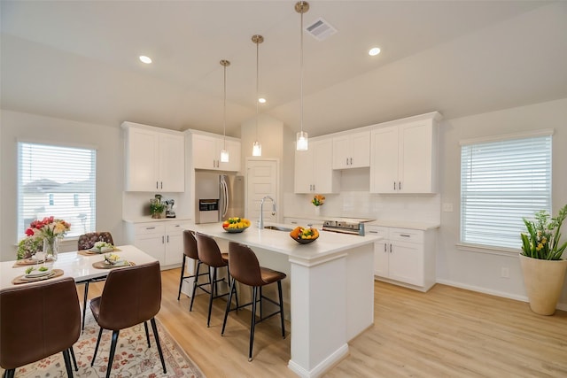 kitchen featuring sink, stainless steel appliances, white cabinets, a center island with sink, and decorative light fixtures