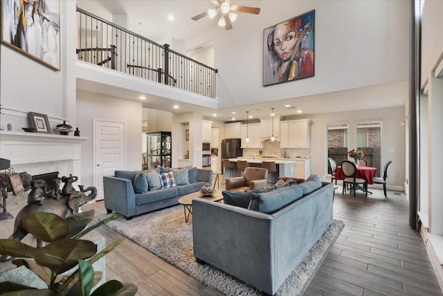 living room with a tile fireplace, ceiling fan, dark hardwood / wood-style flooring, and a towering ceiling