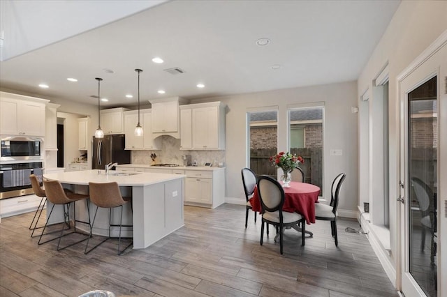 kitchen featuring appliances with stainless steel finishes, wood-type flooring, a center island with sink, white cabinets, and hanging light fixtures