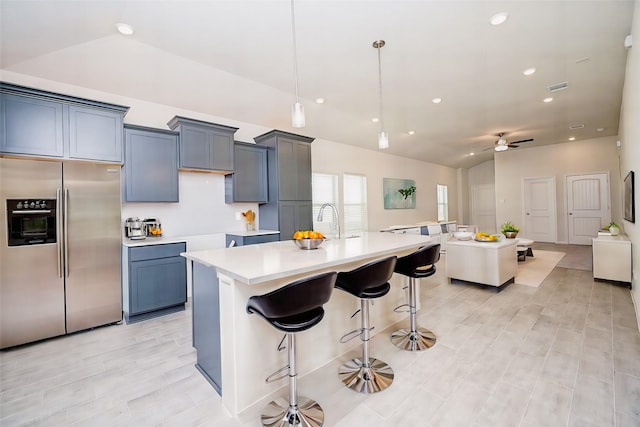 kitchen with pendant lighting, a breakfast bar, a center island with sink, vaulted ceiling, and stainless steel fridge