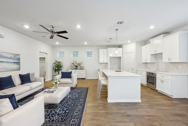 kitchen with sink, a kitchen island with sink, white cabinets, decorative light fixtures, and stainless steel oven