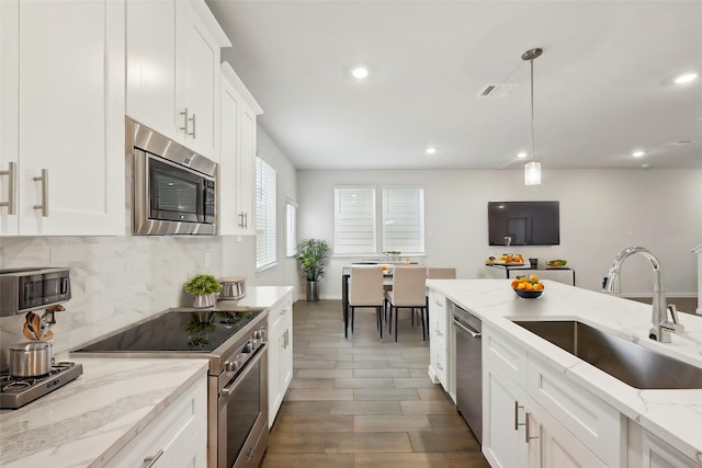 kitchen with appliances with stainless steel finishes, pendant lighting, white cabinetry, sink, and light stone counters