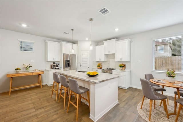 kitchen with white cabinets, a kitchen island with sink, and stainless steel fridge