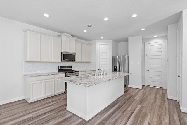 kitchen featuring decorative backsplash, stainless steel appliances, a kitchen island with sink, white cabinets, and light hardwood / wood-style floors