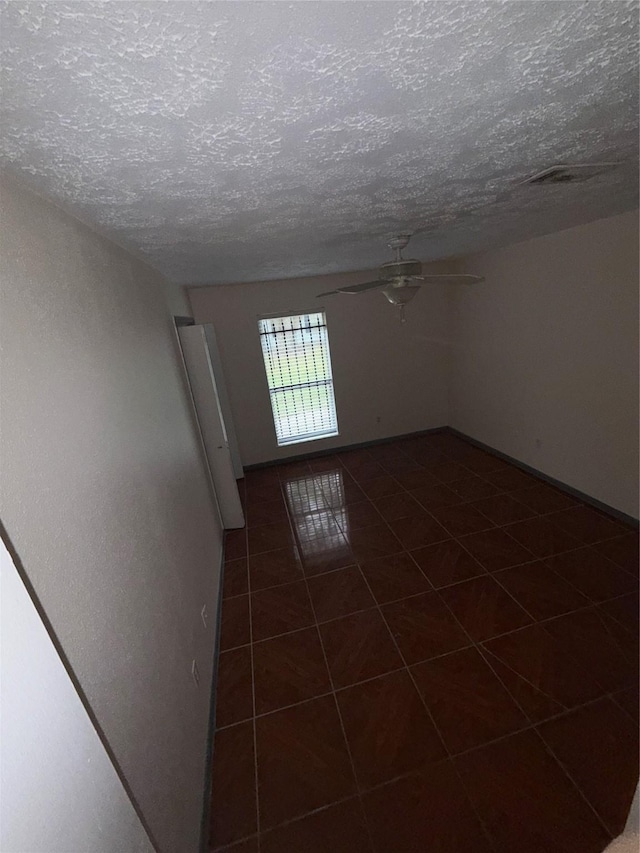 tiled empty room with ceiling fan and a textured ceiling