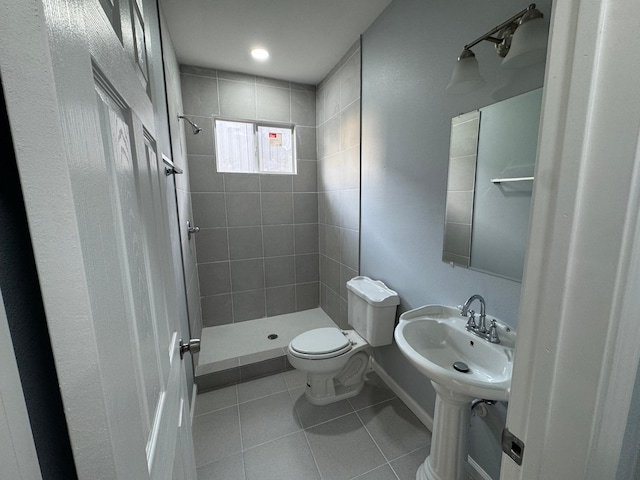 bathroom with tile patterned flooring, a tile shower, toilet, and sink