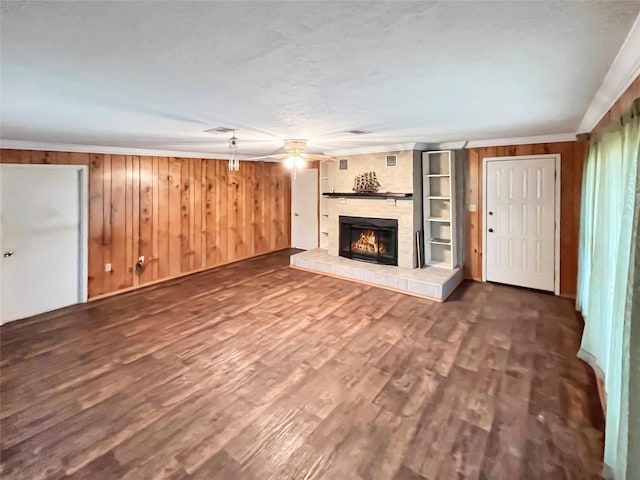 unfurnished living room with wood walls, crown molding, dark hardwood / wood-style floors, and a brick fireplace