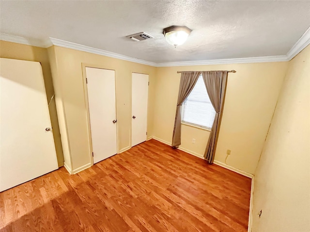 unfurnished bedroom featuring a textured ceiling, light hardwood / wood-style flooring, and ornamental molding