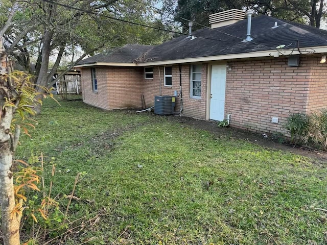 rear view of house with central air condition unit and a lawn