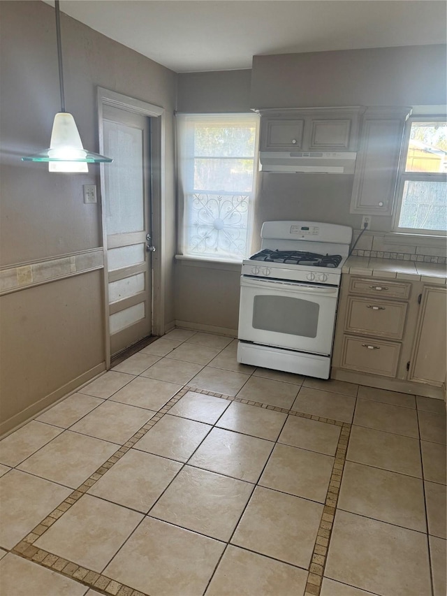 kitchen with pendant lighting, white gas range oven, light tile patterned floors, tile counters, and white cabinetry