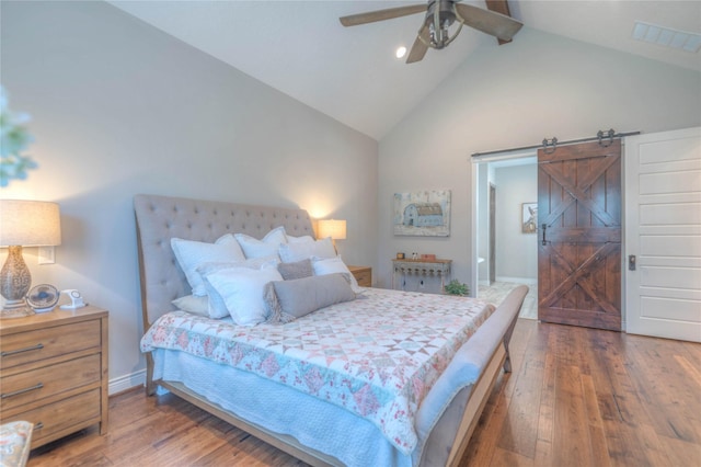 bedroom with hardwood / wood-style flooring, ceiling fan, a barn door, and high vaulted ceiling