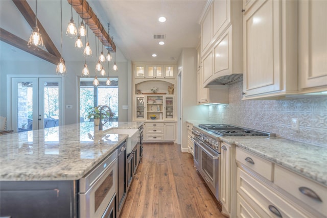 kitchen with light stone countertops, french doors, sink, high end stainless steel range oven, and light wood-type flooring